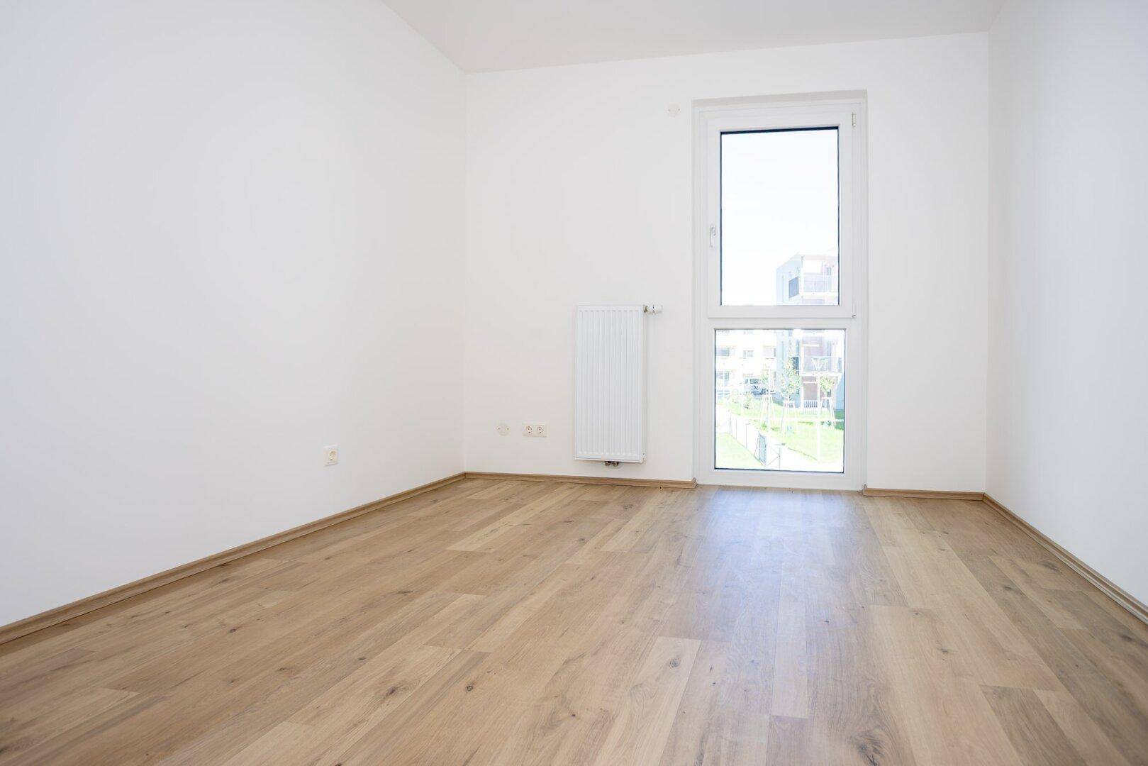 Geräumiges Zimmer mit Laminatboden, großen Fenstern und Blick auf die grüne Umgebung.