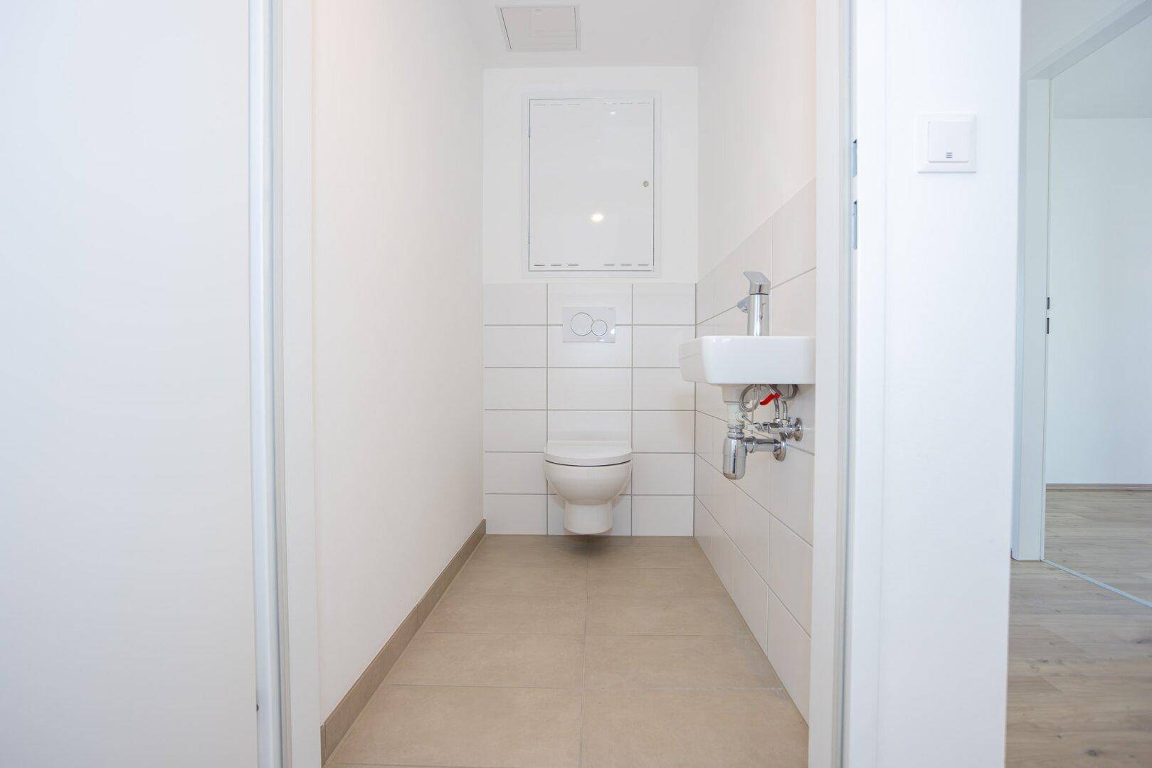 Kleines Gäste-WC mit Wand-WC, Handwaschbecken und weißen Wandfliesen.