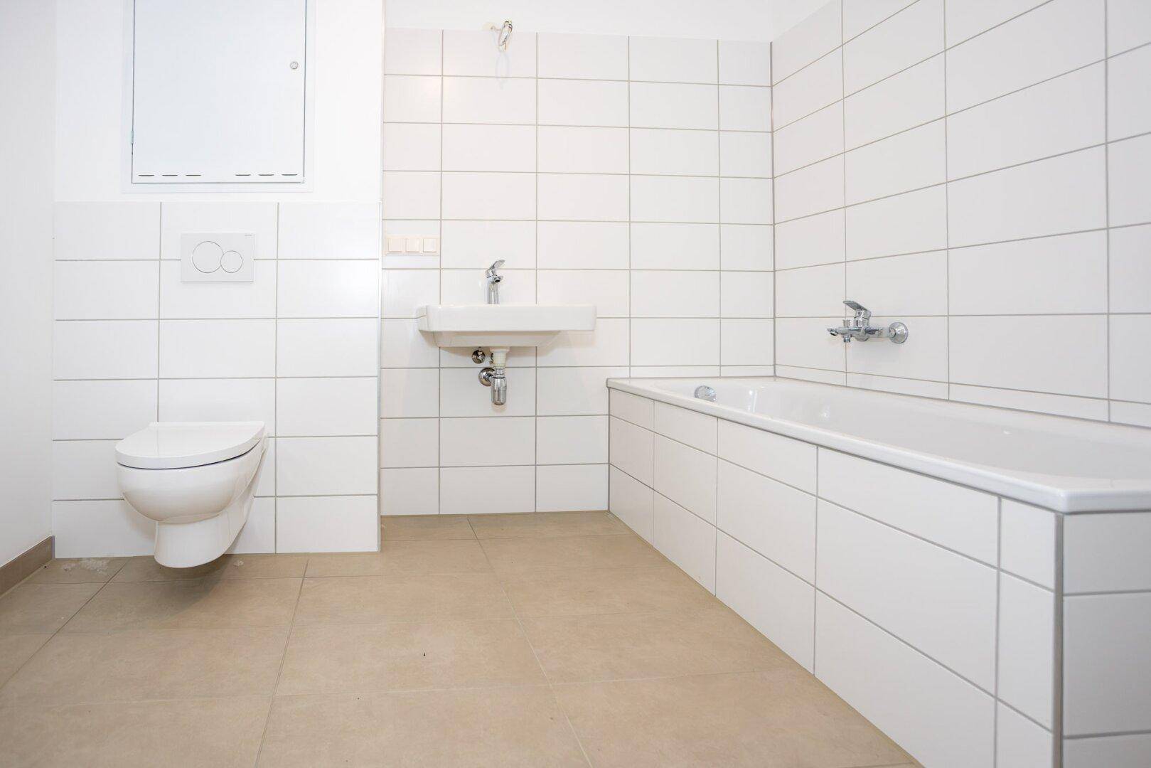 Modernes Badezimmer mit weißen Fliesen, Badewanne, Waschbecken und wandhängendem WC.