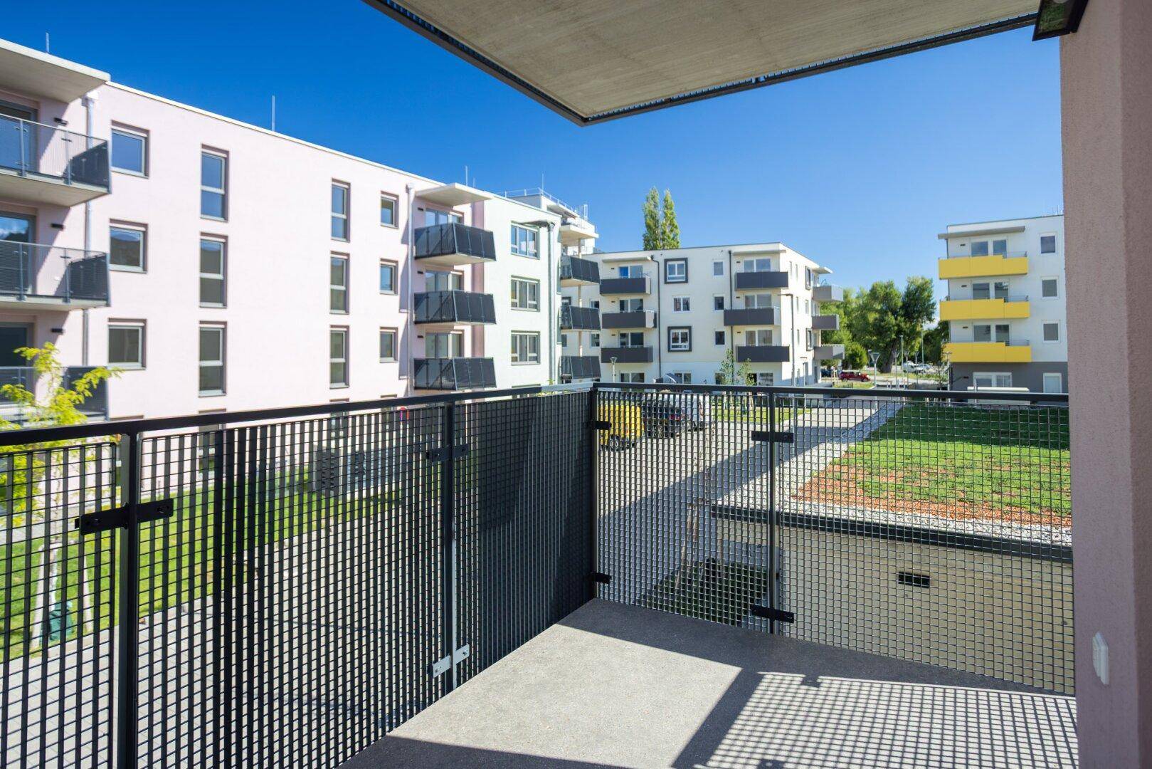 Sonniger Balkon mit Blick auf die umliegenden Neubauten und den gepflegten Innenhofbereich.