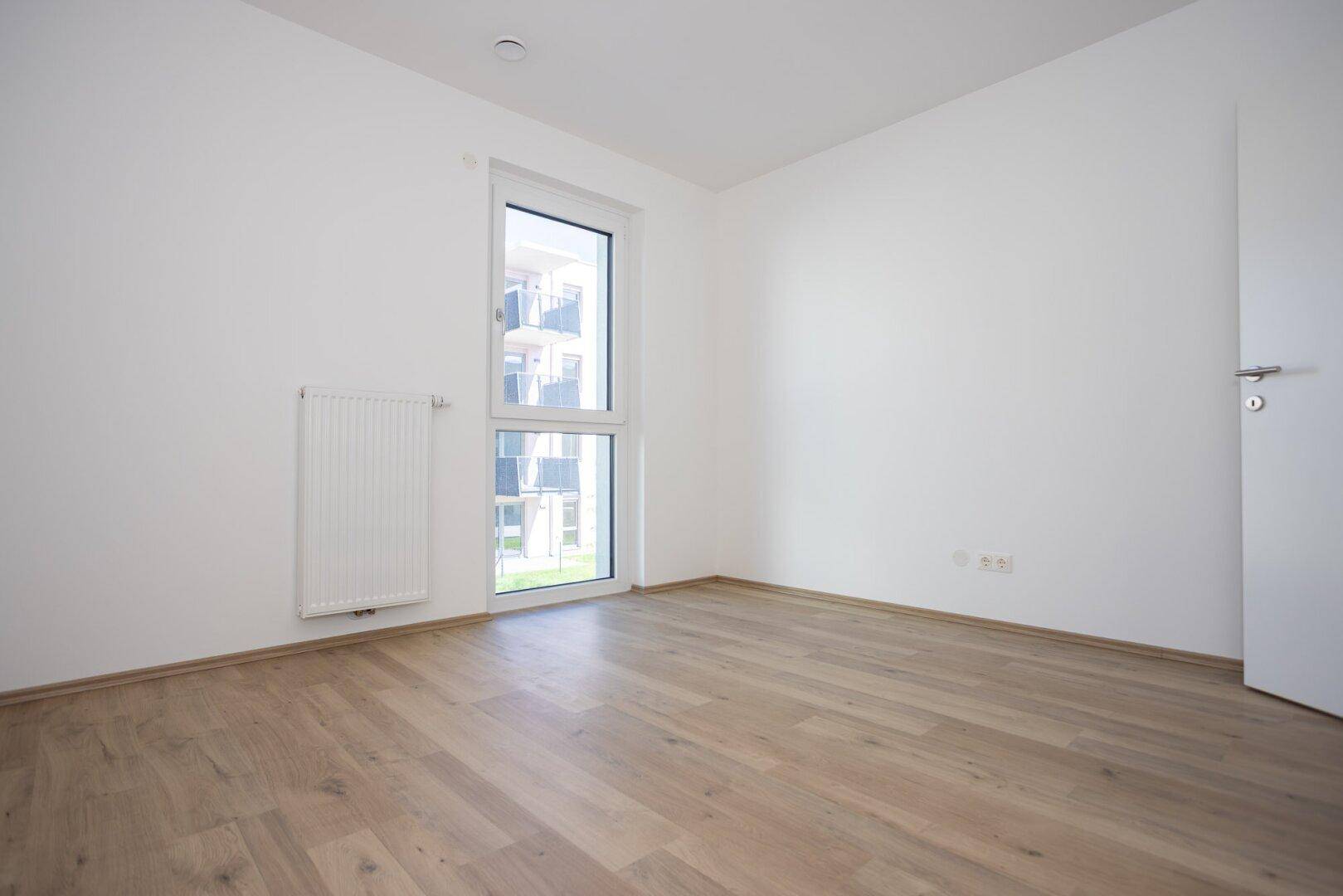 Ruhiges Schlafzimmer mit Holzboden und Fenster, das einen Blick nach draußen bietet.