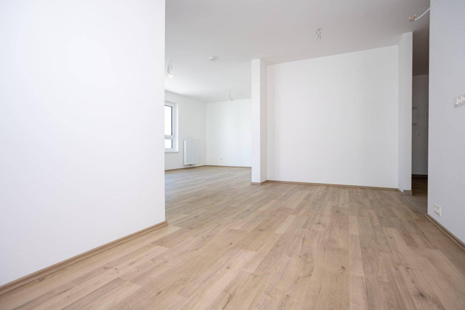 Offener Wohnbereich mit hellem Holzboden und weißen Wänden, bereit zur individuellen Gestaltung.