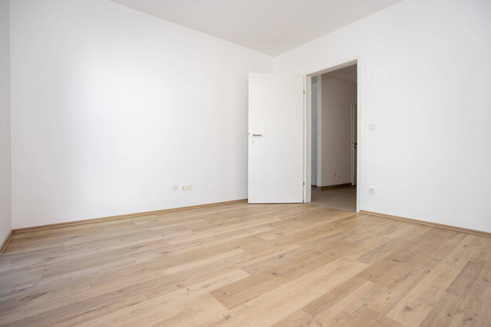 Leeres Zimmer mit Holzboden und weiß gestrichenen Wänden, bereit für neue Bewohner.