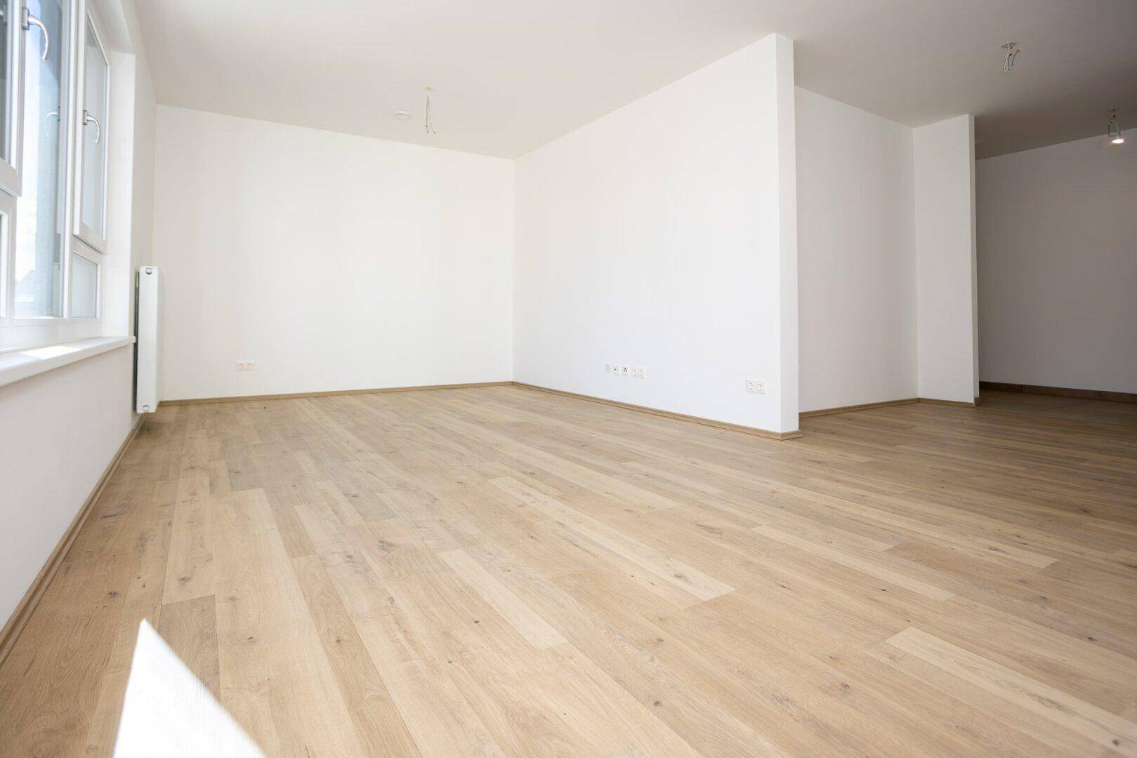 Geräumiger, heller Raum mit Holzboden und großen Fenstern, ideal für offenes Wohnen.