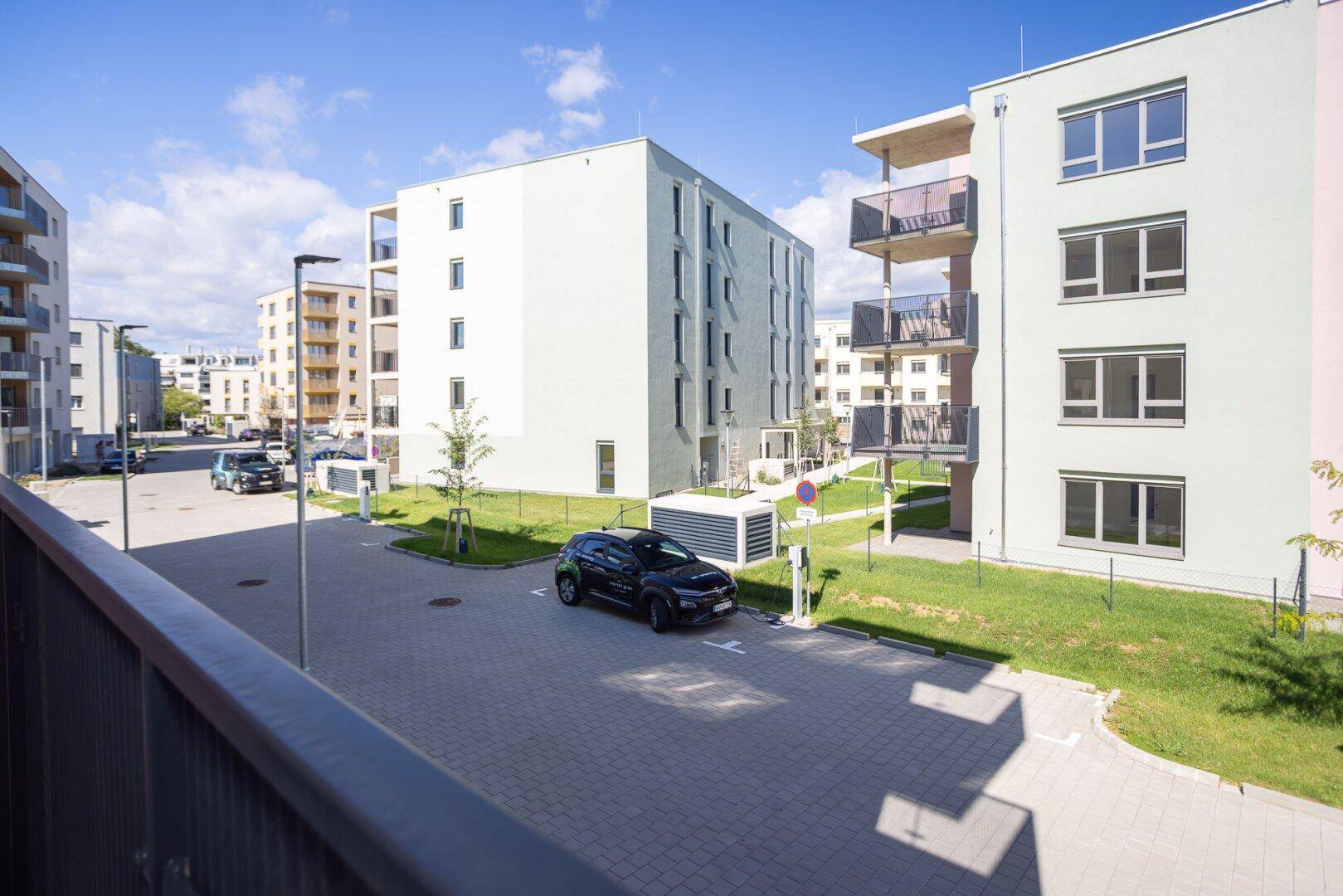 Außenansicht der modernen Wohnanlage mit Parkplätzen und Grünflächen unter blauem Himmel.