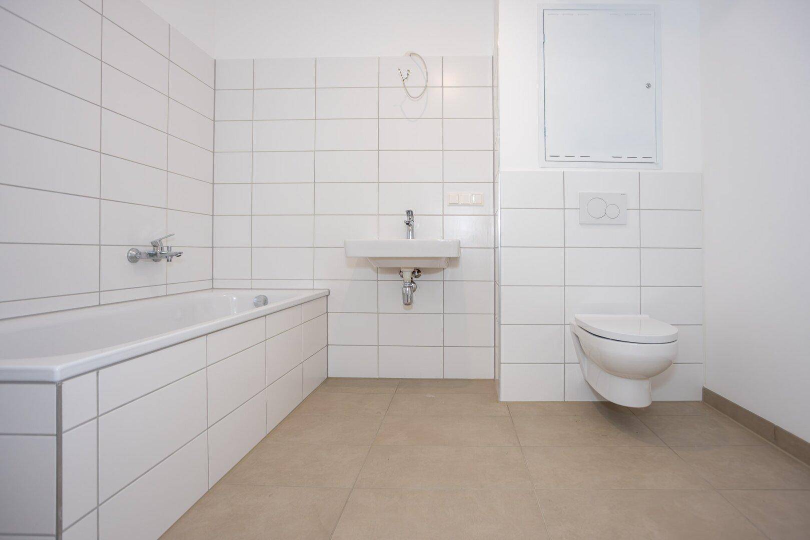 Modernes Badezimmer mit weißen Fliesen, Badewanne und wandhängendem WC.