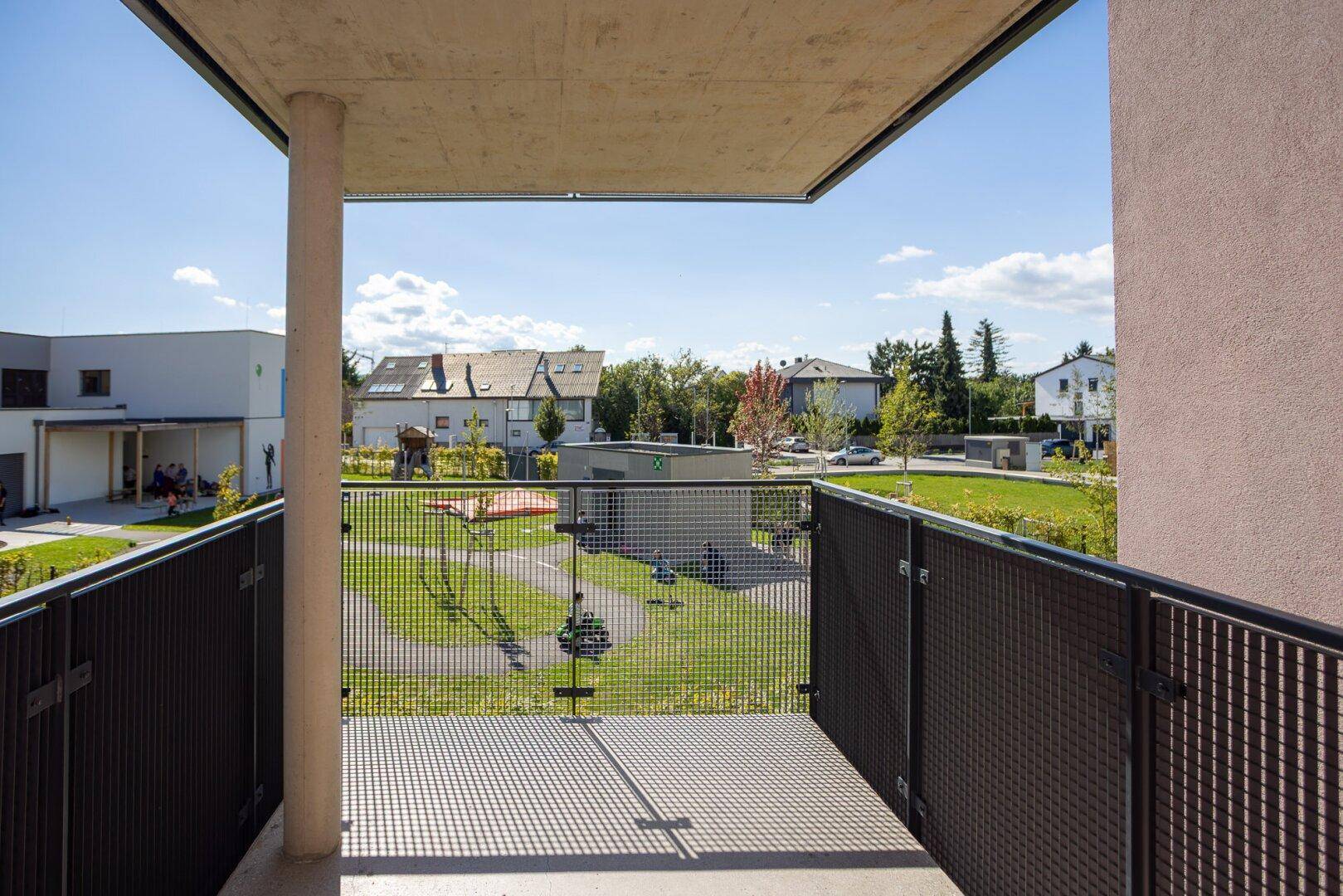 Balkon mit Blick auf eine Grünfläche und umliegende Wohngebäude.