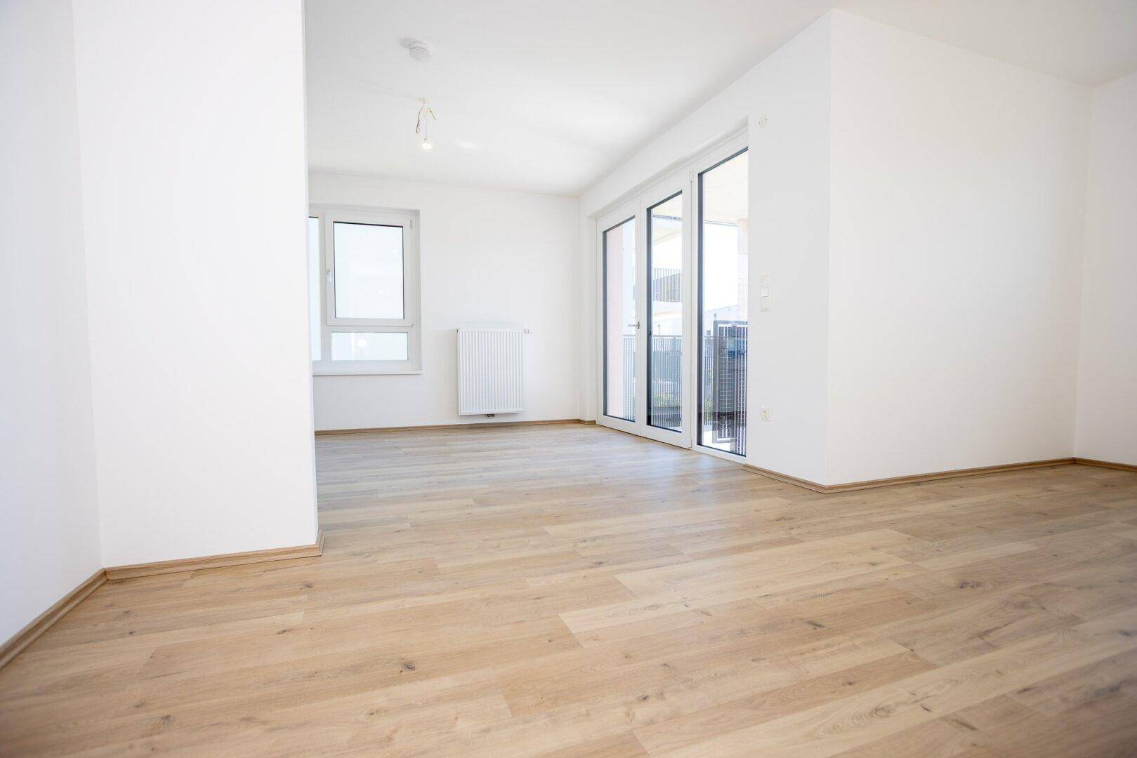 Heller Wohnraum mit Laminatboden und Zugang zu einem Balkon.