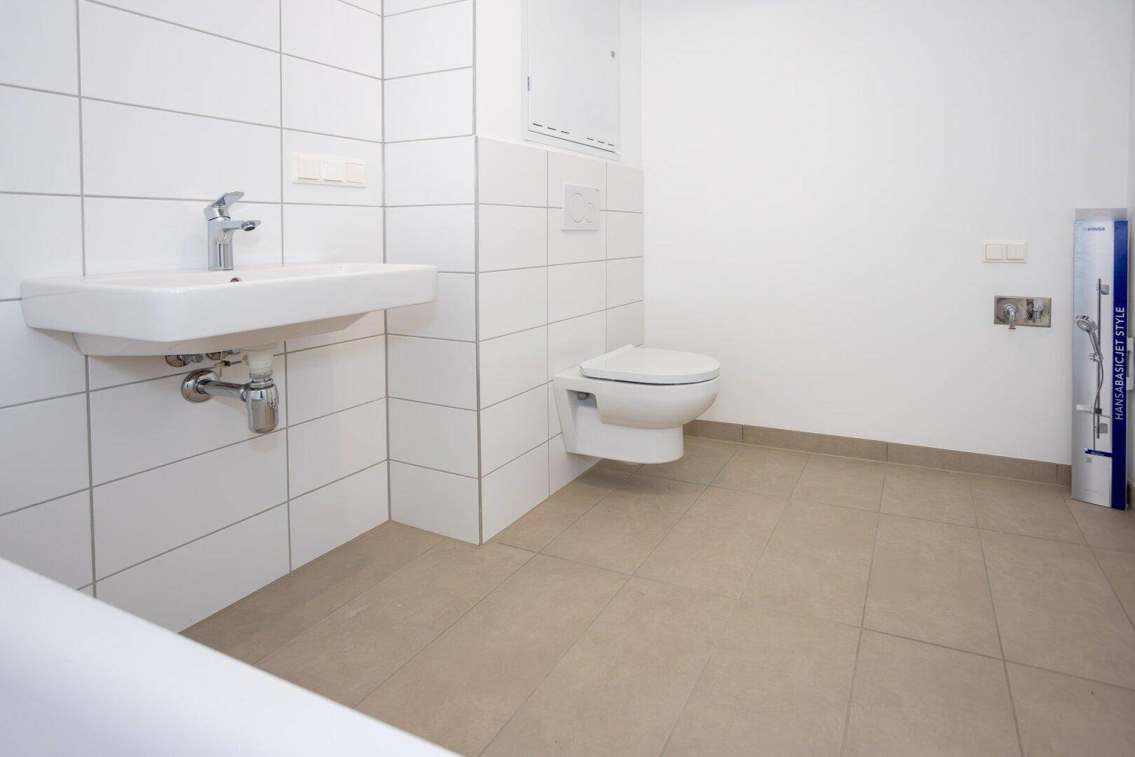 Helles Badezimmer mit weißen Wandfliesen, Waschbecken und wandhängendem WC.