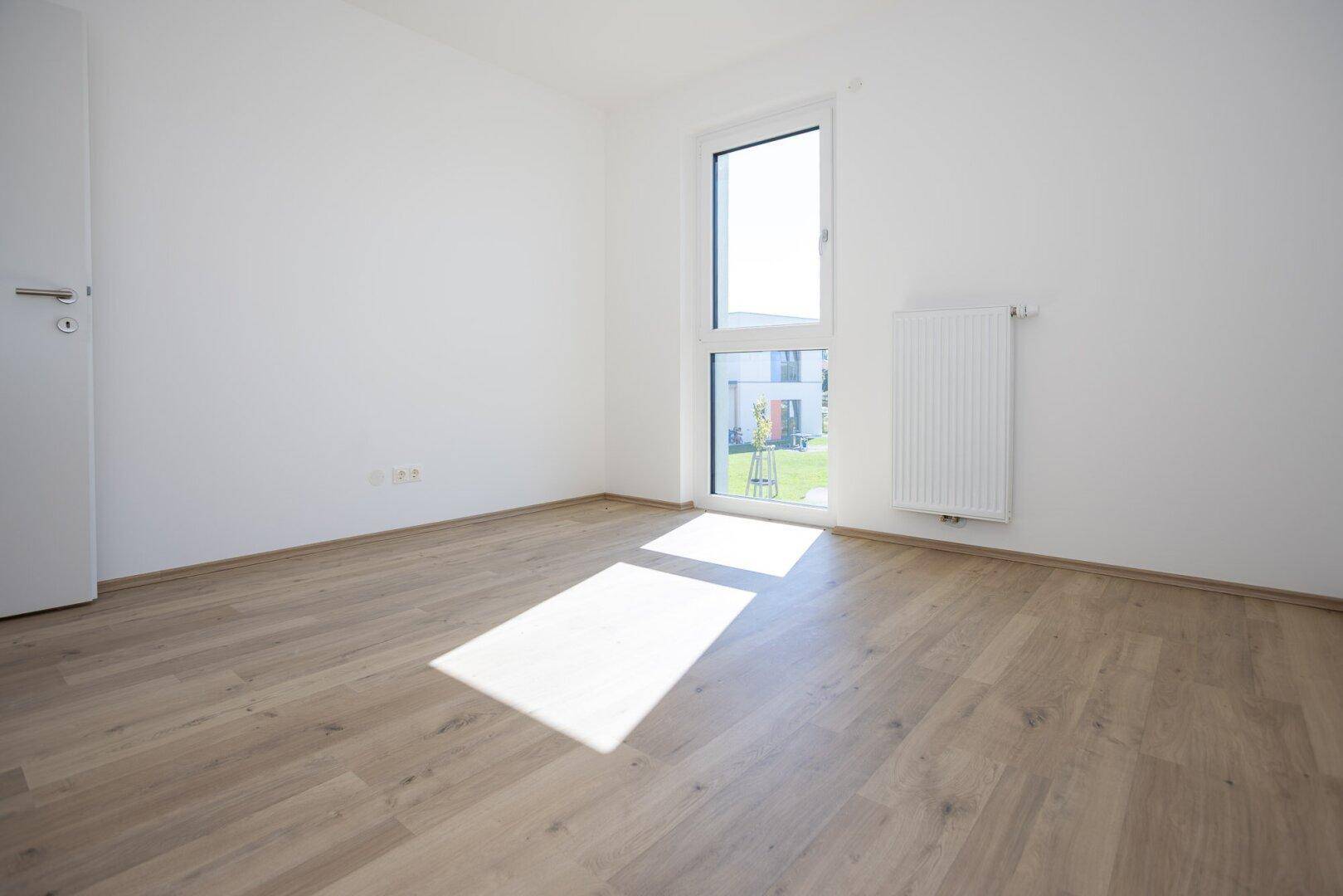 Geräumiges Schlafzimmer mit hellem Laminatboden und einem hohen Fenster.