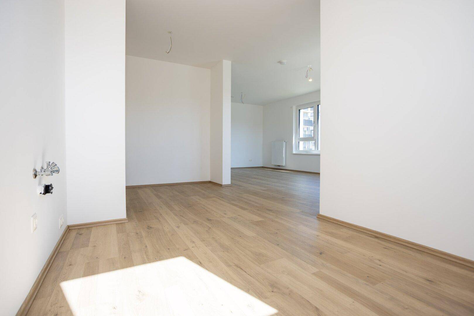 Leerer Raum mit hellem Laminatboden und weiß gestrichenen Wänden.