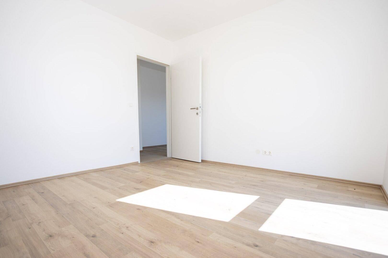 Leeres Schlafzimmer mit Laminatboden und weiß gestrichenen Wänden.