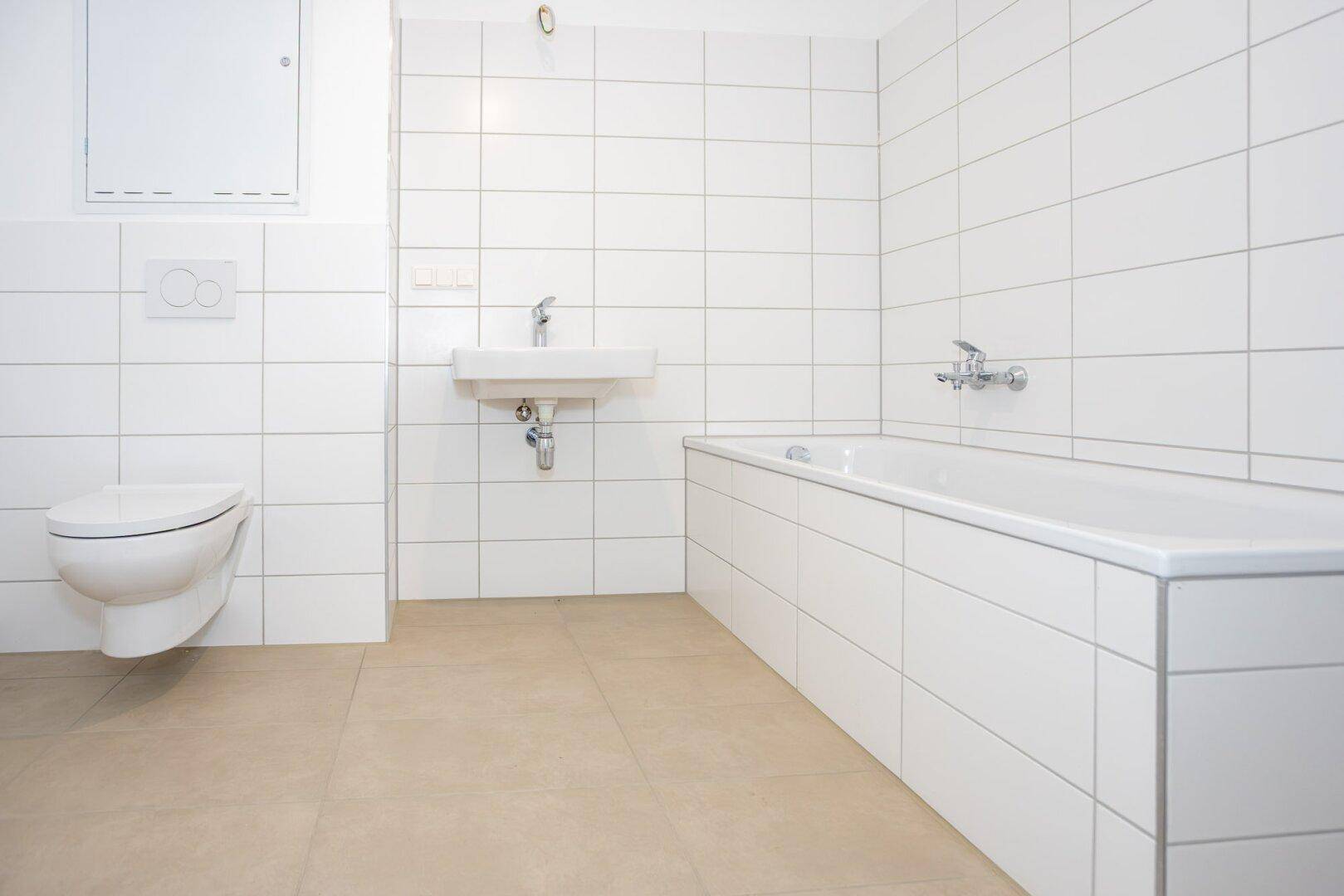 Modernes Badezimmer mit weißen Fliesen, Badewanne und wandhängendem WC.