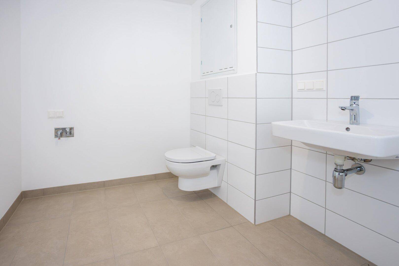 Helles Badezimmer mit weißen Fliesen, Waschbecken und wandhängendem WC.