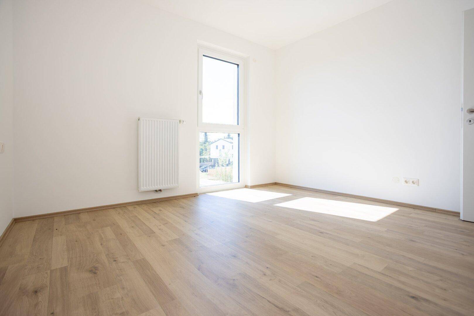 Leeres Zimmer mit Holzboden und Fenster, gut beleuchtet durch natürliches Tageslicht.