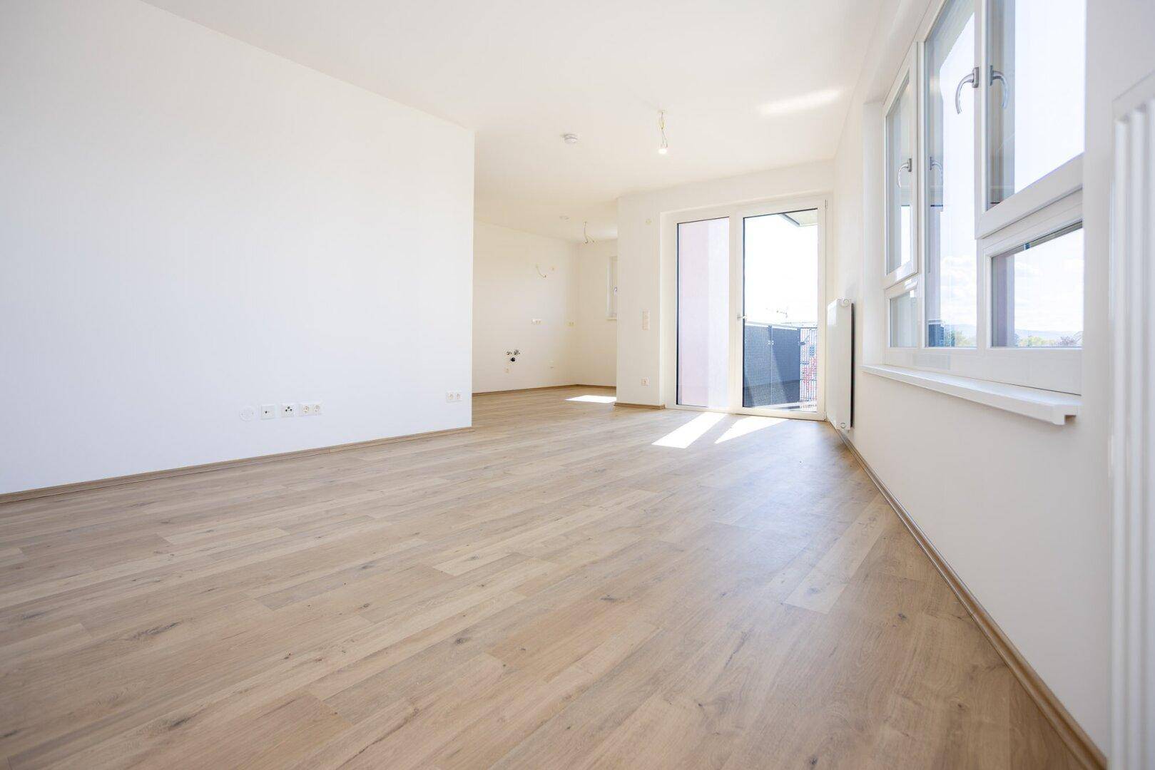 Geräumiges, helles Wohnzimmer mit Holzboden und großen Fenstern, bereit zur Einrichtung.
