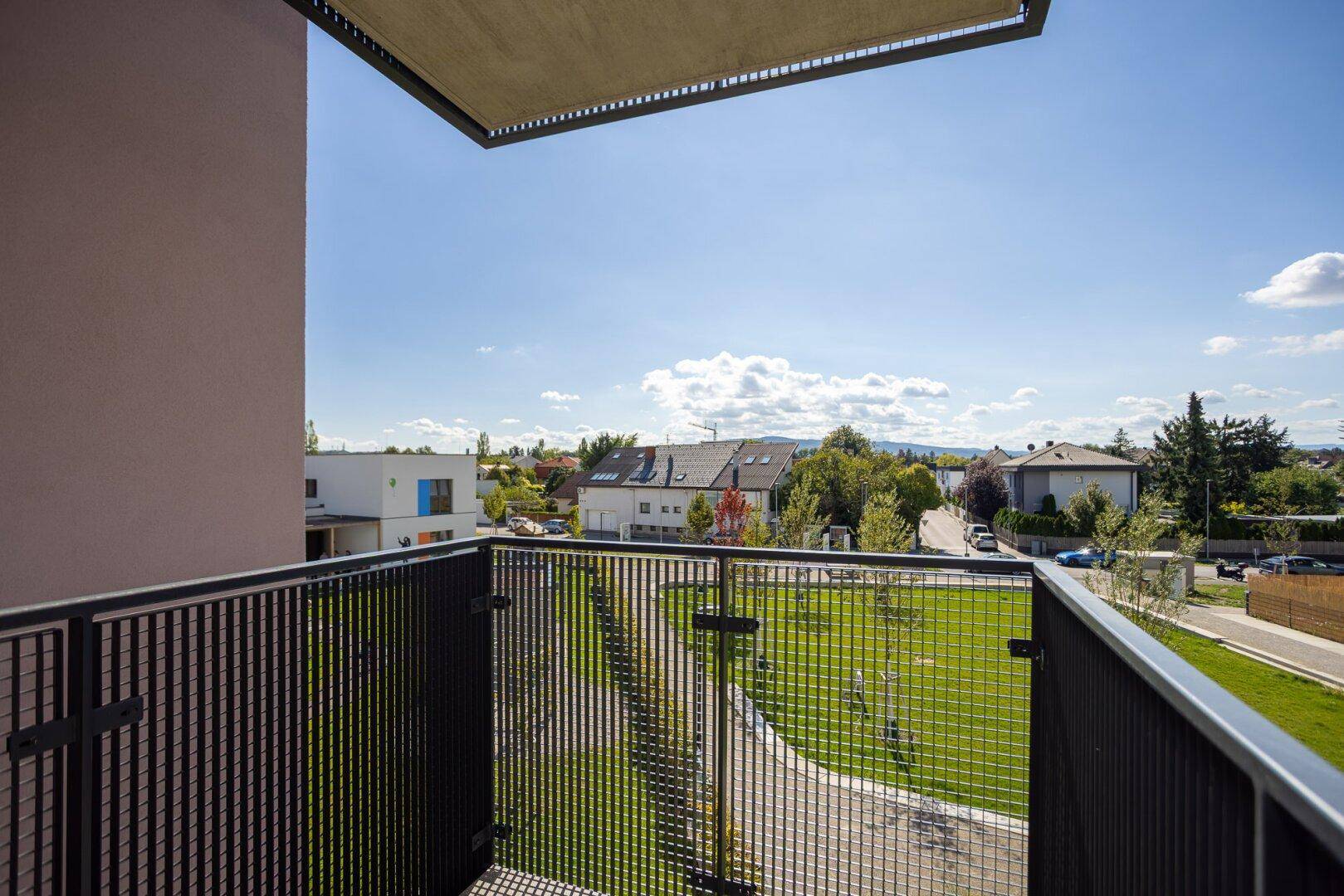 Balkon mit Blick auf die grüne Umgebung und Wohngebäude unter blauem Himmel.