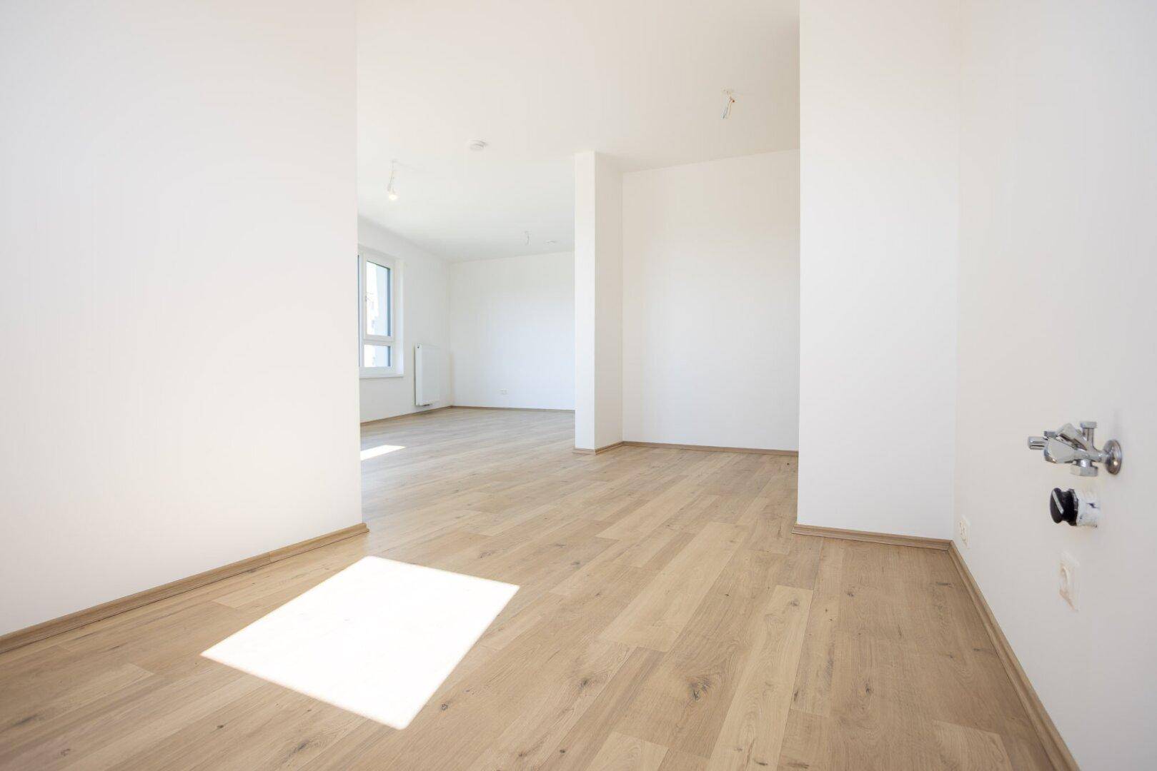 Heller Innenraum mit Holzboden und sichtbaren Anschlüssen an der Wand, möglicherweise für eine Küche.