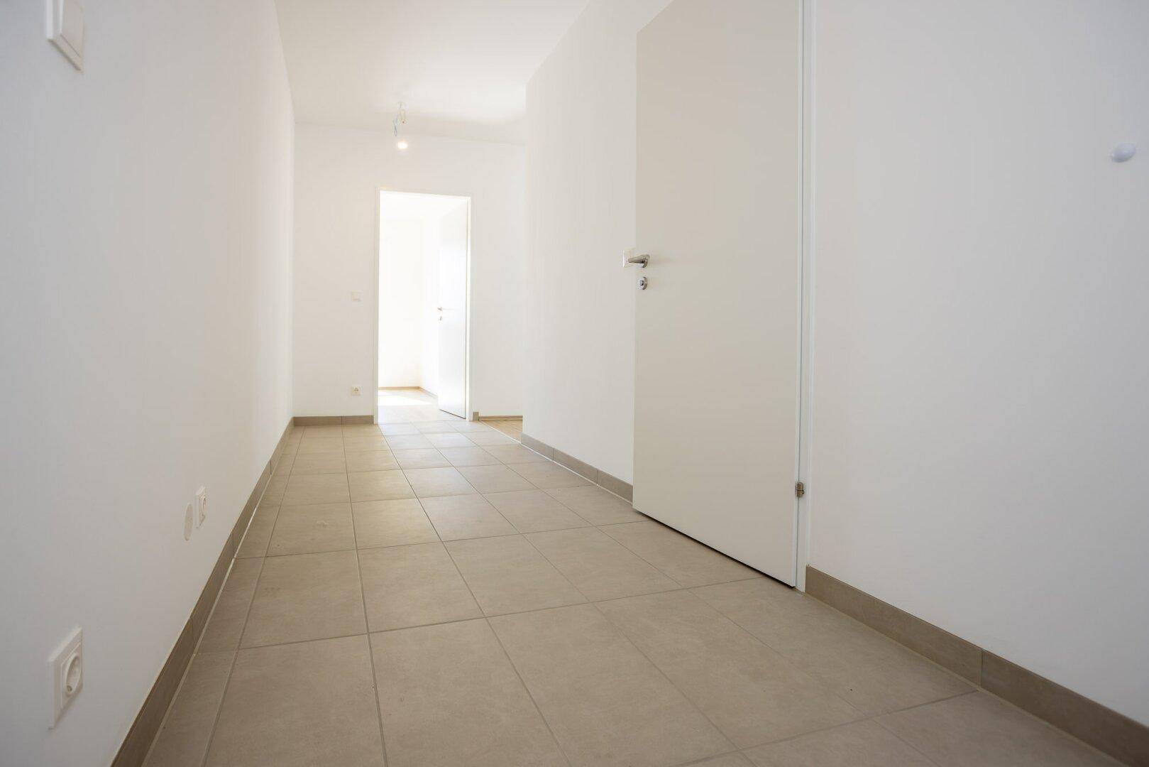 Heller Flur mit Fliesenboden und weißen Wänden, führt zu weiteren Räumen.