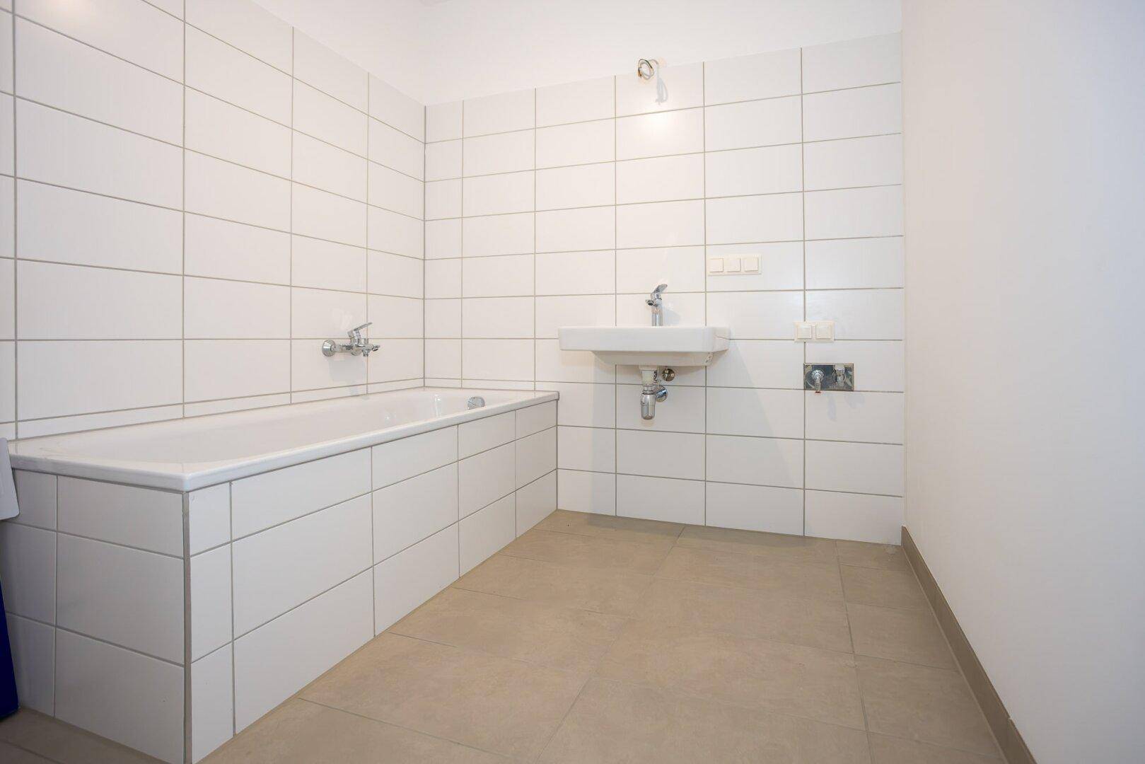 Modernes Badezimmer mit Badewanne, Waschbecken und weißen Fliesen an den Wänden.