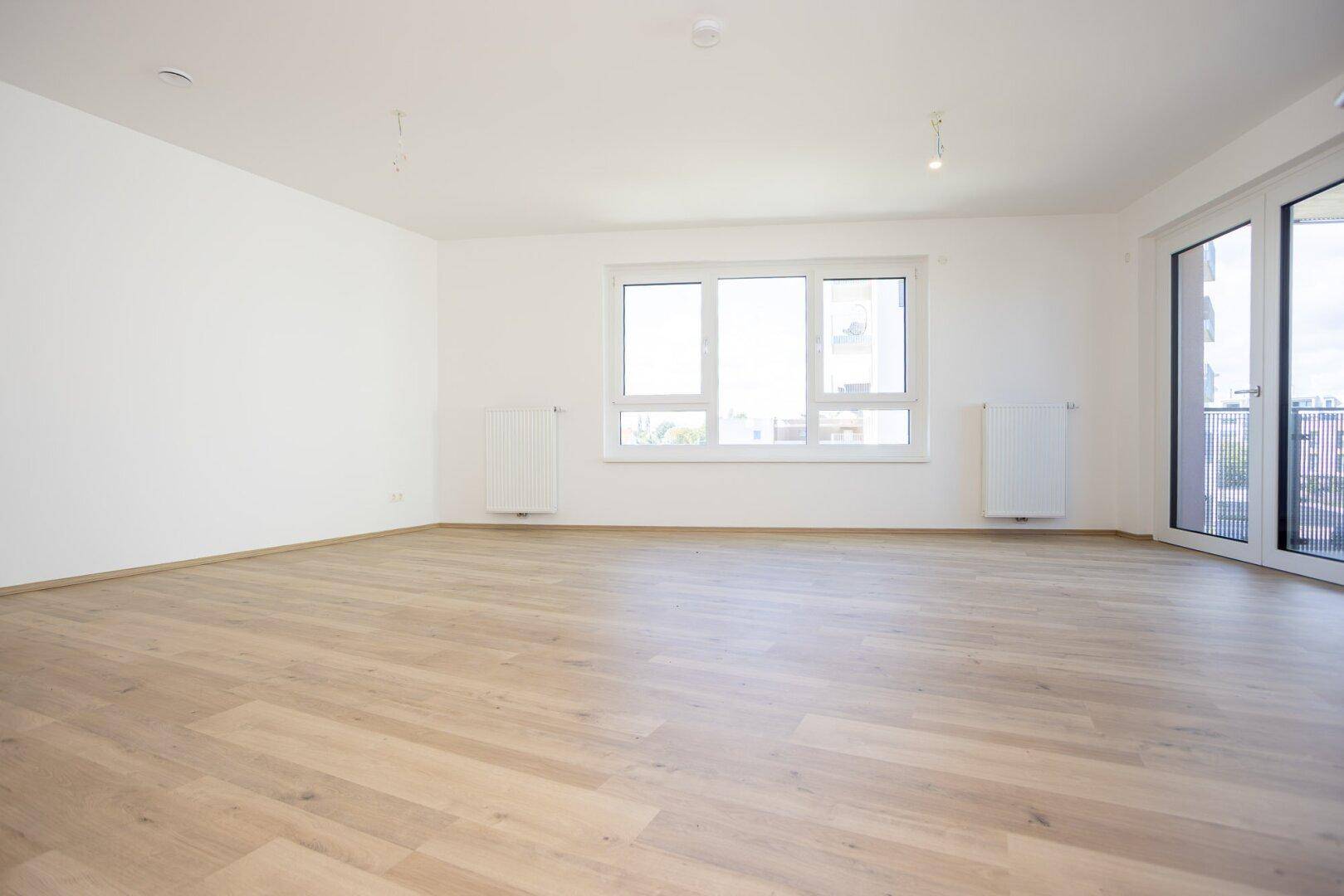 Weitläufiges Wohnzimmer mit großen Fenstern, viel Tageslicht und hellem Laminatboden.