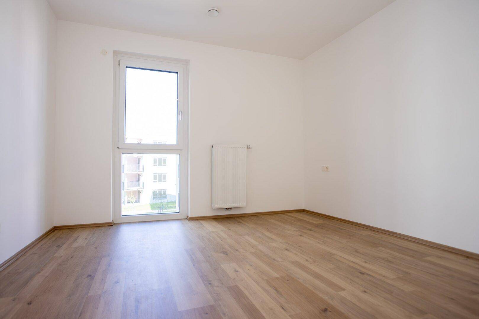 Helles Schlafzimmer mit großem Fenster, Heizkörper und neuem Laminatboden.