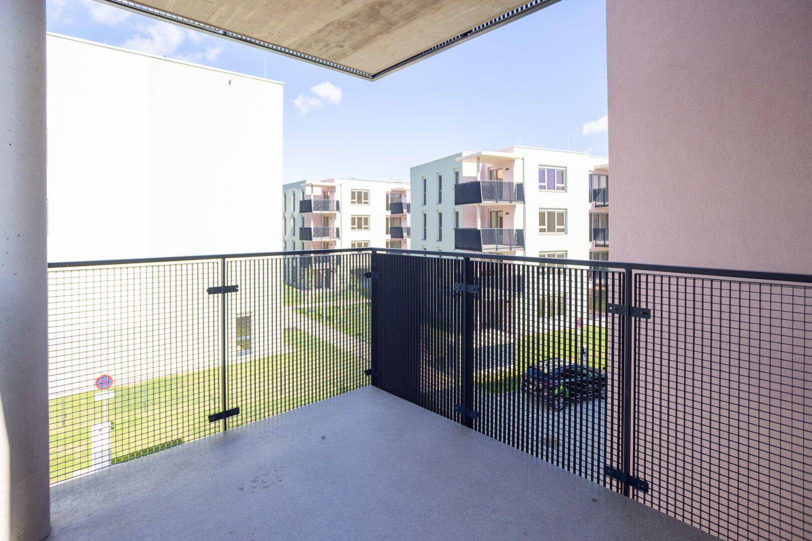 Geräumiger Balkon mit Gittergeländer und Ausblick auf die Wohnanlage.