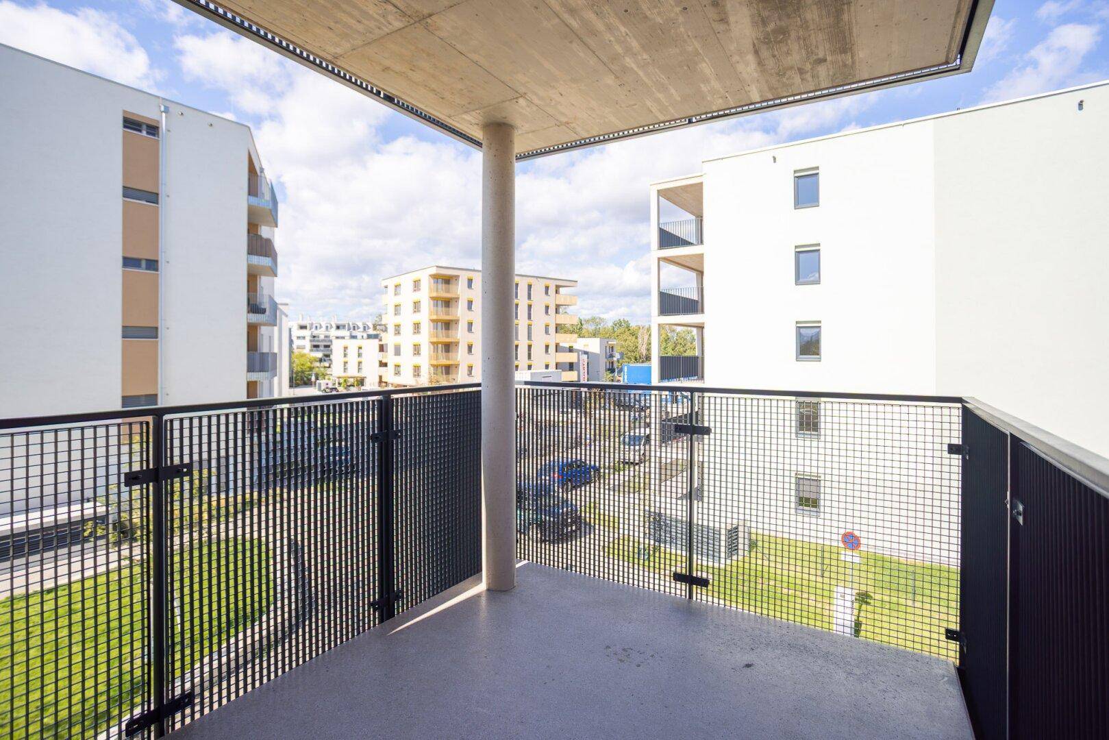 Heller Balkon mit Betonstütze und weitem Blick über die moderne Wohnsiedlung.