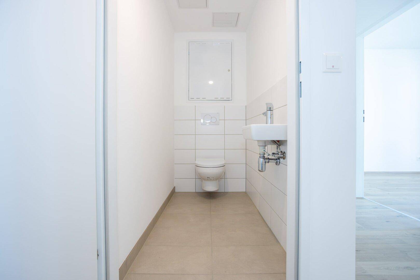 Separates Gäste-WC mit wandhängender Toilette, kleinem Waschbecken und weißen Fliesen.