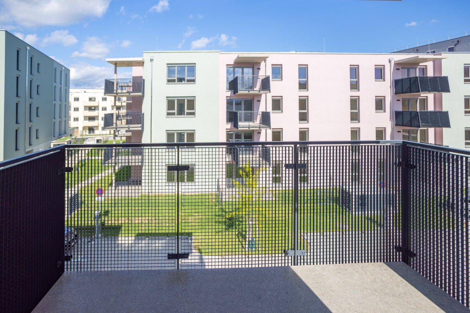 Balkon mit Gittergeländer und Blick auf den grünen Innenhof der Wohnanlage.