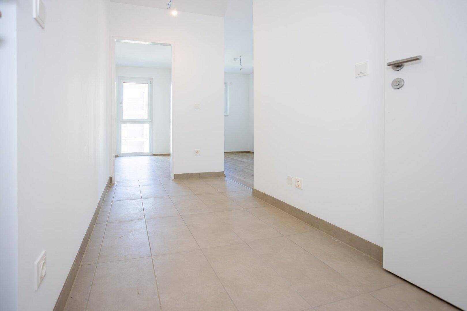 Heller Flur mit Fliesenboden, der zu den verschiedenen Räumen der Wohnung führt.