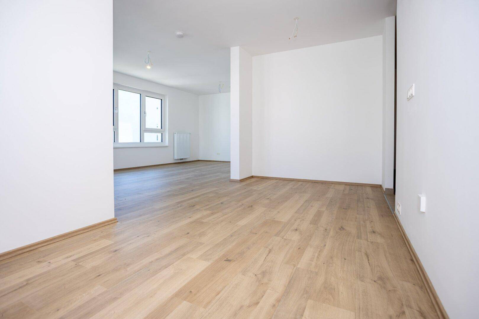 Heller Flur mit Holzboden, der in einen offenen Wohnbereich übergeht.