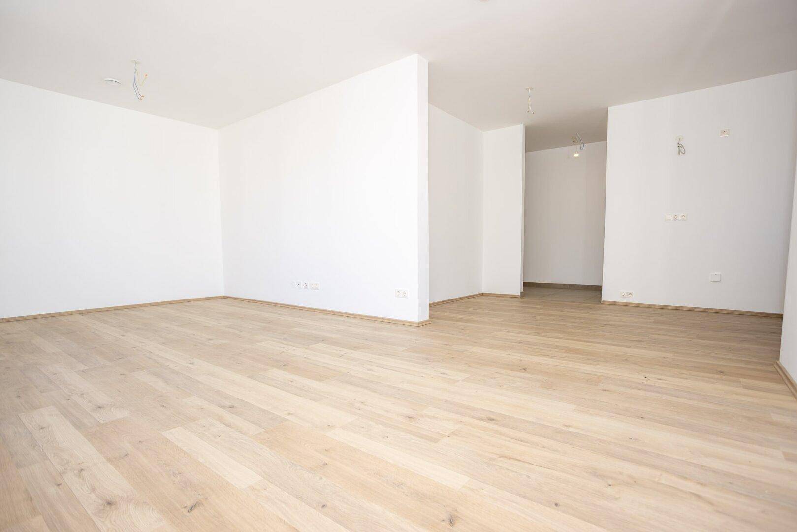 Offener, heller Raum mit Holzboden und weißen Wänden, bereit zur individuellen Gestaltung.
