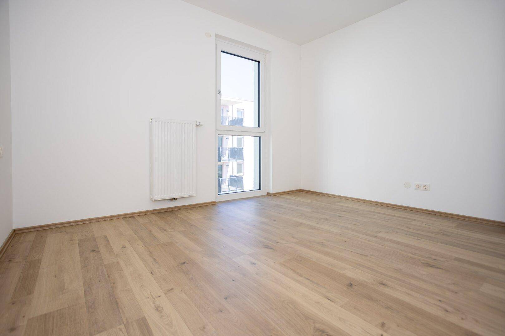 Geräumiges Schlafzimmer mit hellem Holzboden und viel Tageslicht durch die Fenster.