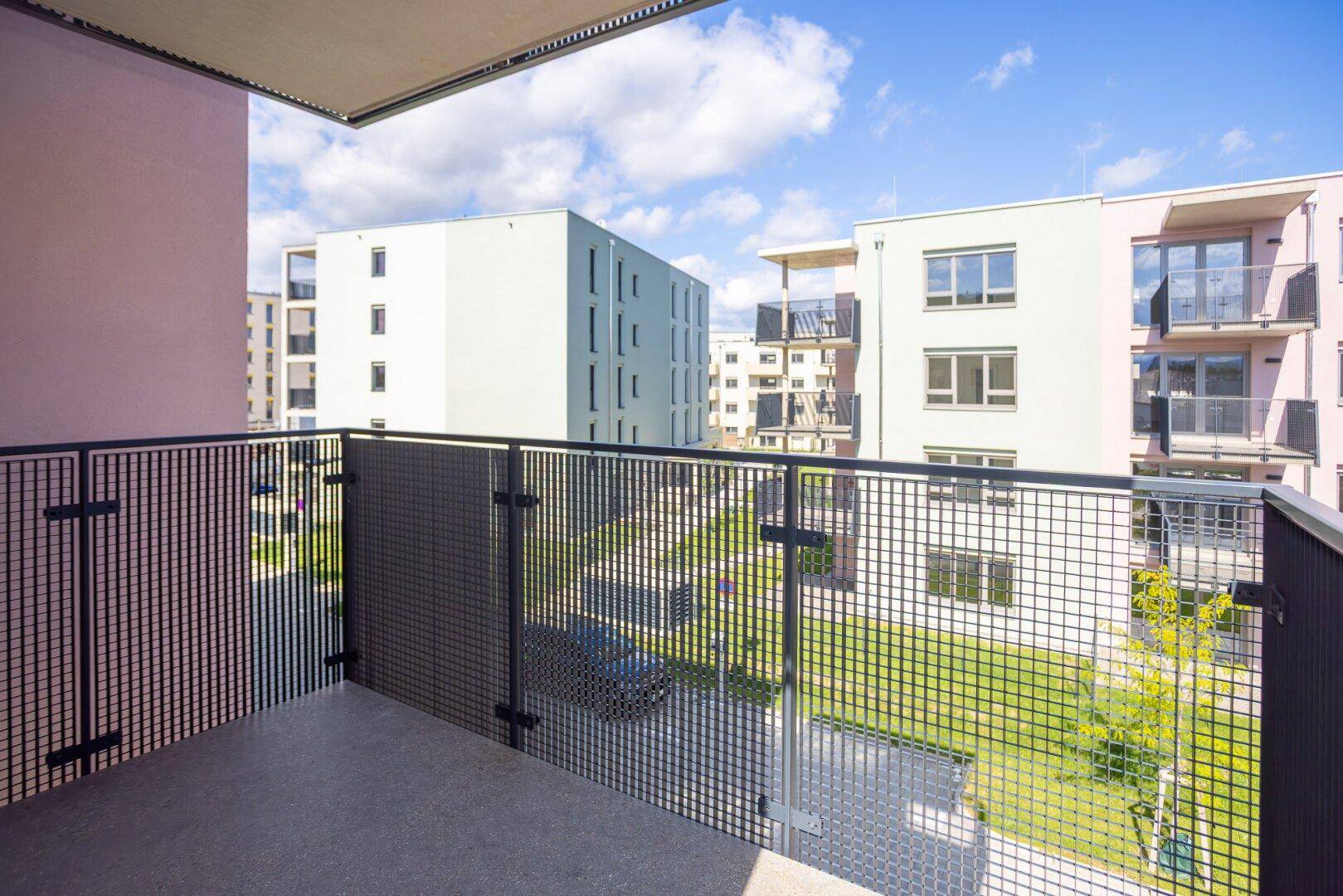 Balkon mit Gittergeländer und Blick auf den begrünten Innenhof der Wohnanlage.