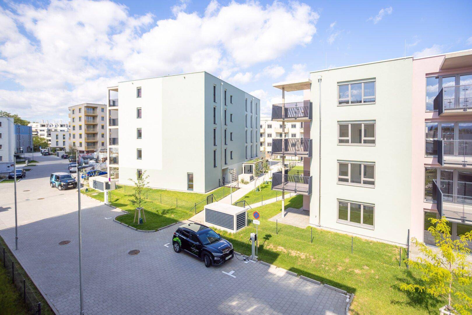 Moderne Wohngebäude mit Grünflächen, Parkplätzen und Ladestationen für Elektrofahrzeuge.