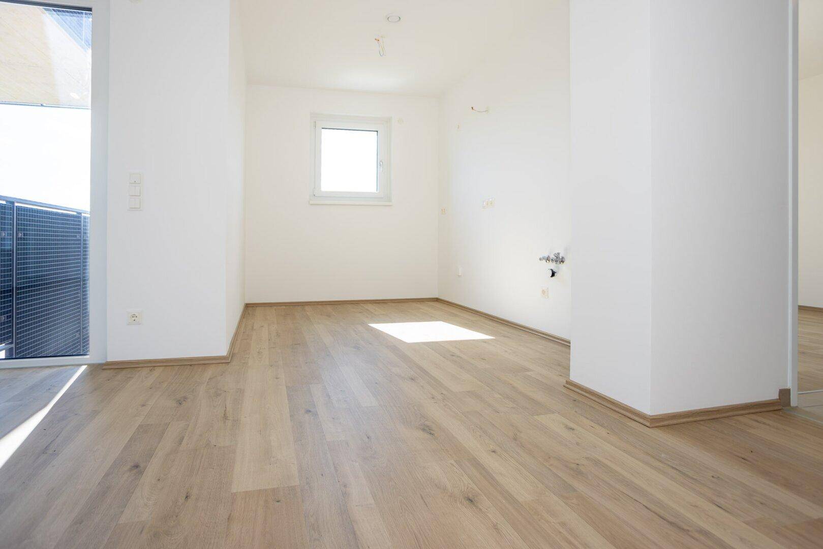 Leerer Raum für eine Küche mit Anschlüssen und hellem Laminatboden.