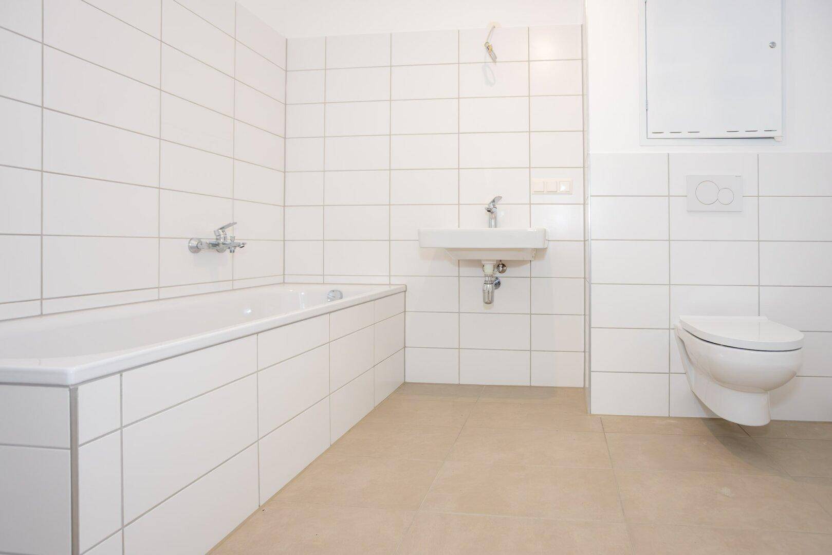 Modernes Badezimmer mit weißen Wandfliesen, Badewanne, Waschbecken und Hänge-WC.