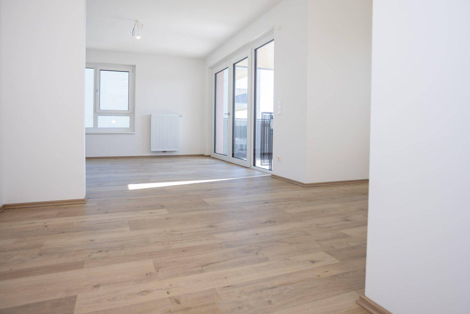 Geräumiger Wohnraum mit viel Tageslicht, hellem Boden und direktem Balkonzugang.