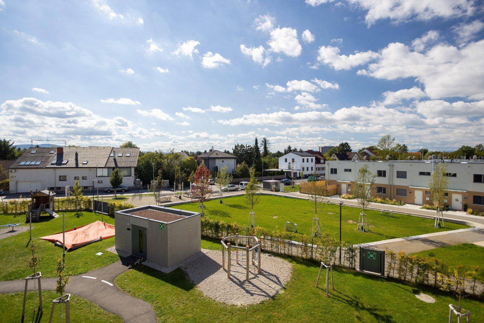 Übersicht über die Wohnanlage mit Grünflächen, Spielplatz und Nebengebäude.
