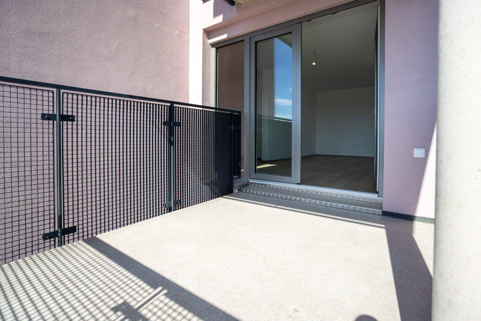 Sonniger Balkon mit Schiebetür zum Wohnbereich und modernem Metallgeländer.