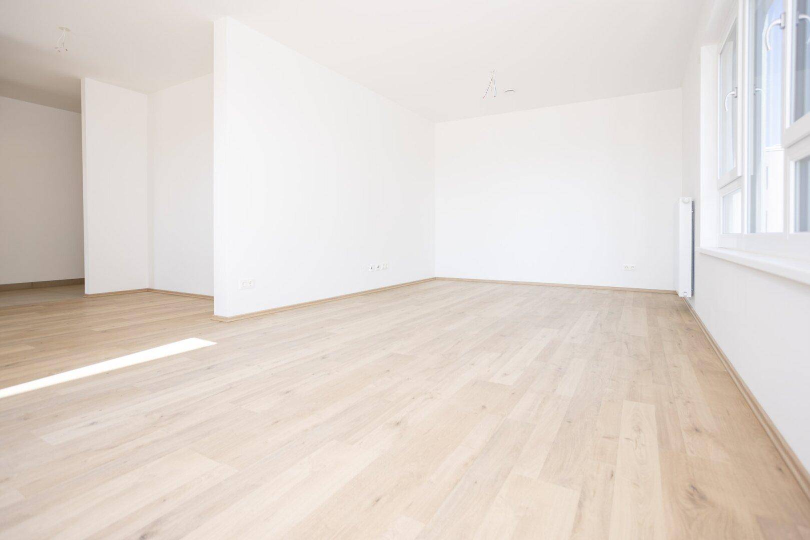Weitläufiger Wohnbereich mit viel Tageslicht und neuwertigem Laminatboden.