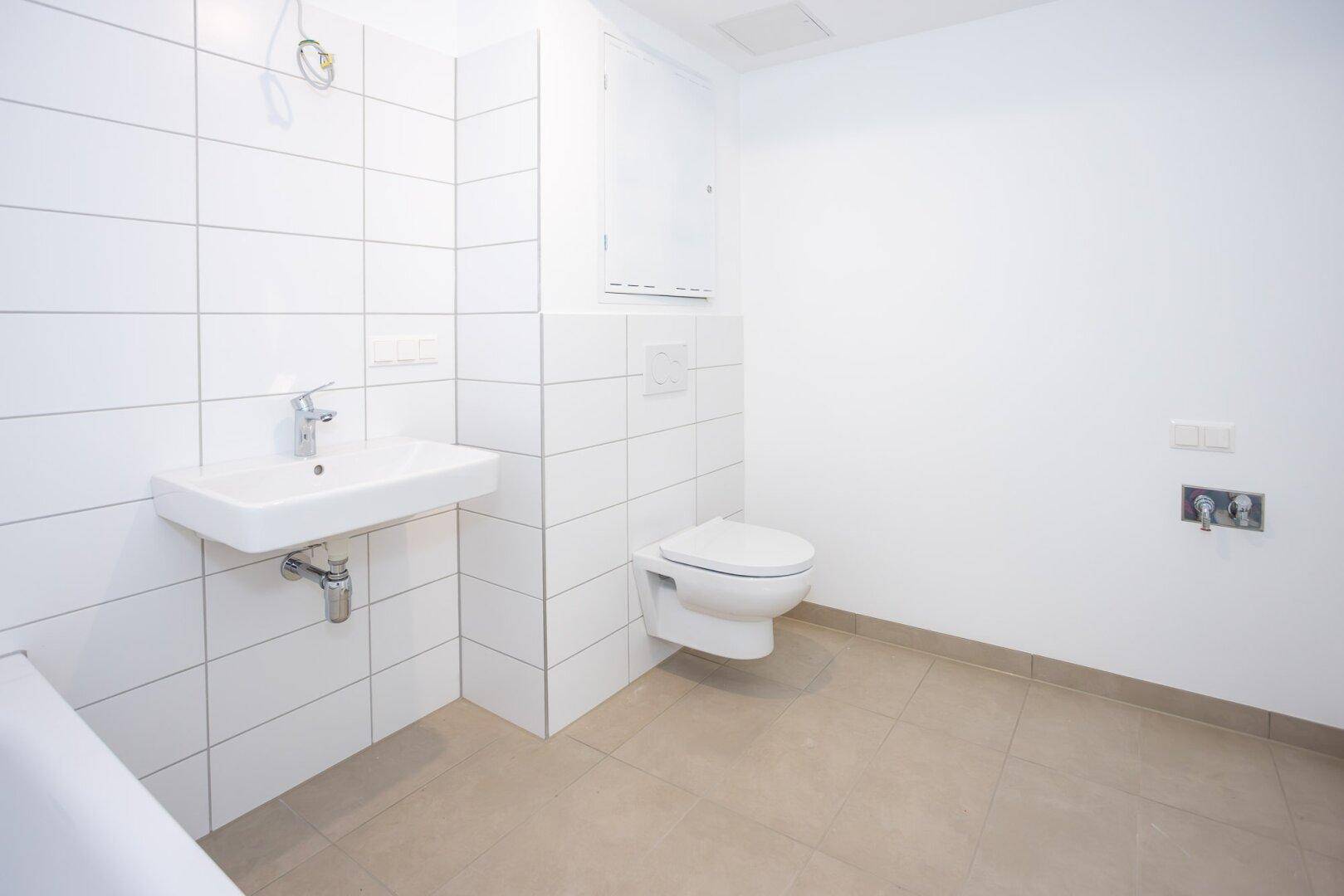Helles Badezimmer mit weißen Fliesen, modernem Waschbecken und wandhängendem WC.