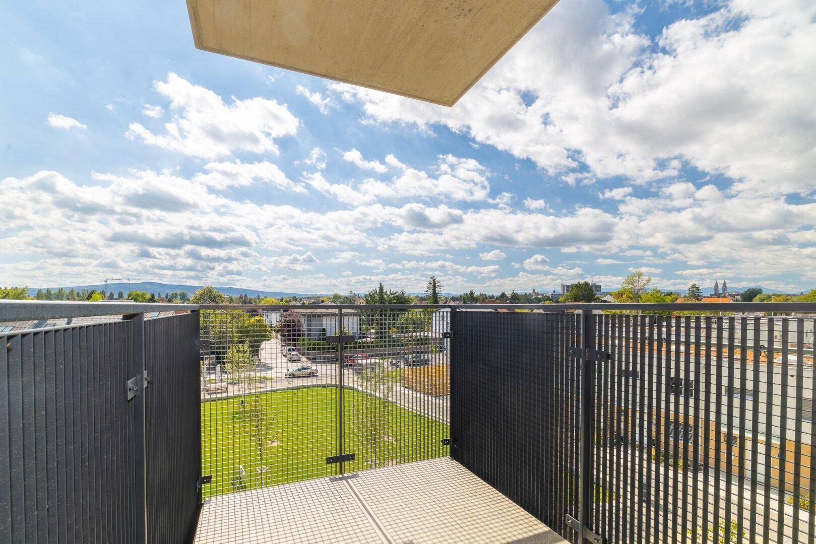 Weitläufiger Blick vom Balkon über die grüne Umgebung und die Dächer der Stadt.