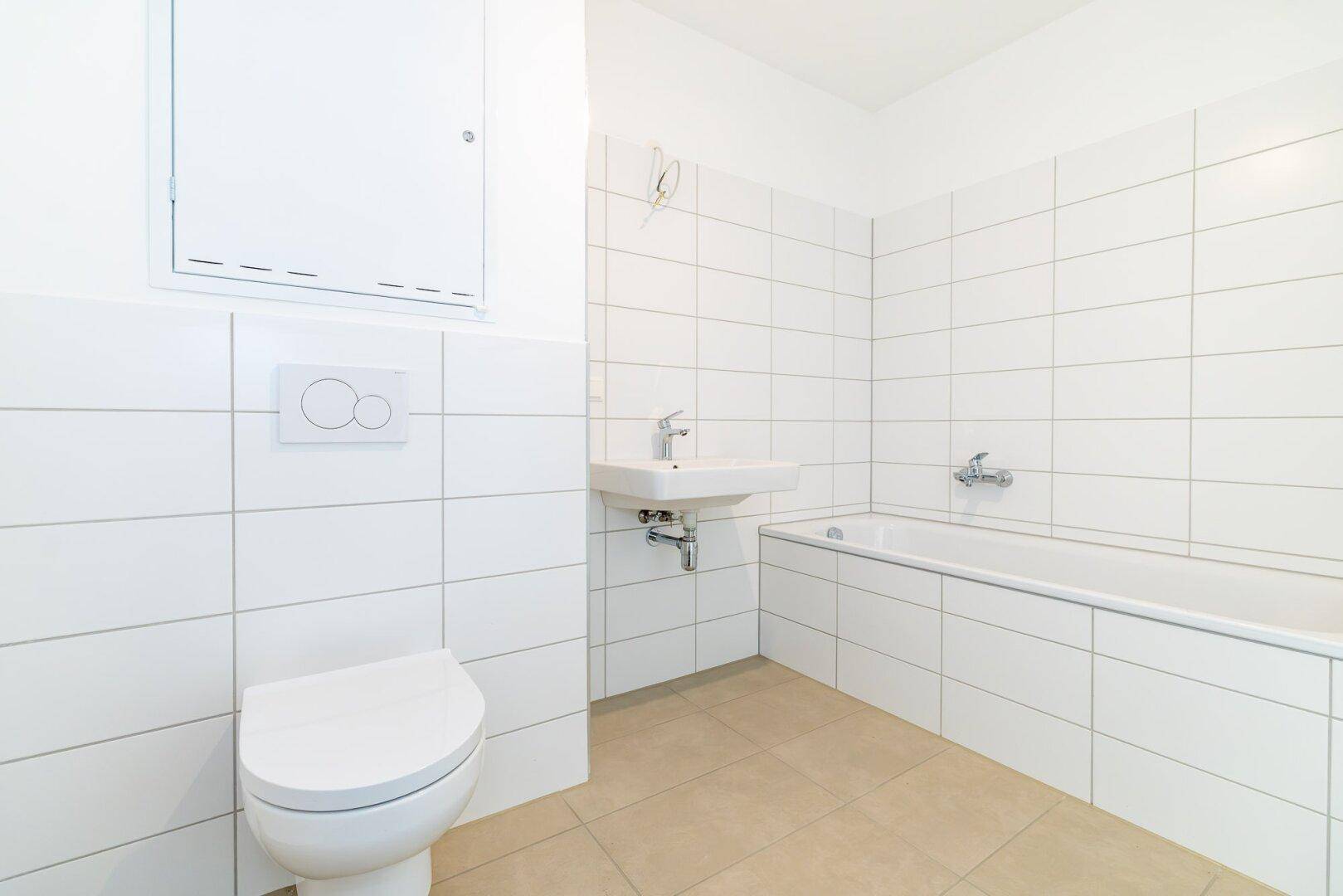 Modern gefliestes Badezimmer mit Badewanne, Toilette und Waschbecken in Weiß und Beige.