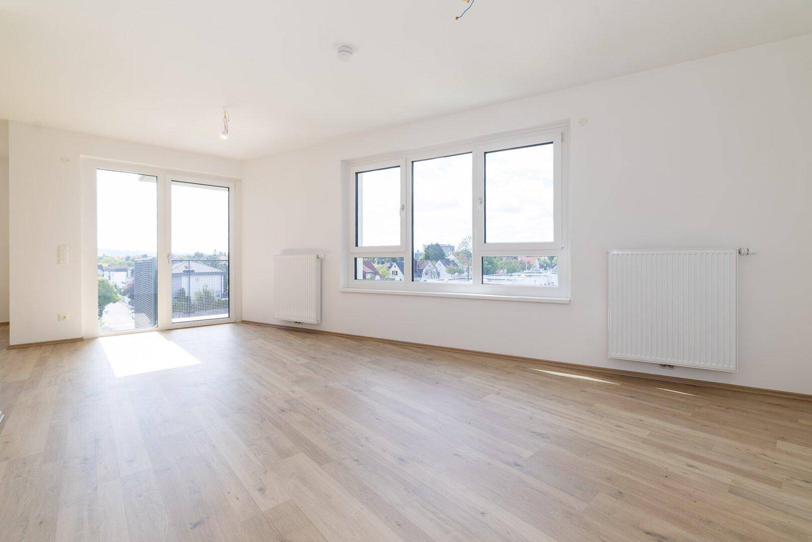 Helles, leeres Zimmer mit großen Fenstern und Zugang zum Balkon, ideal als Wohnbereich.