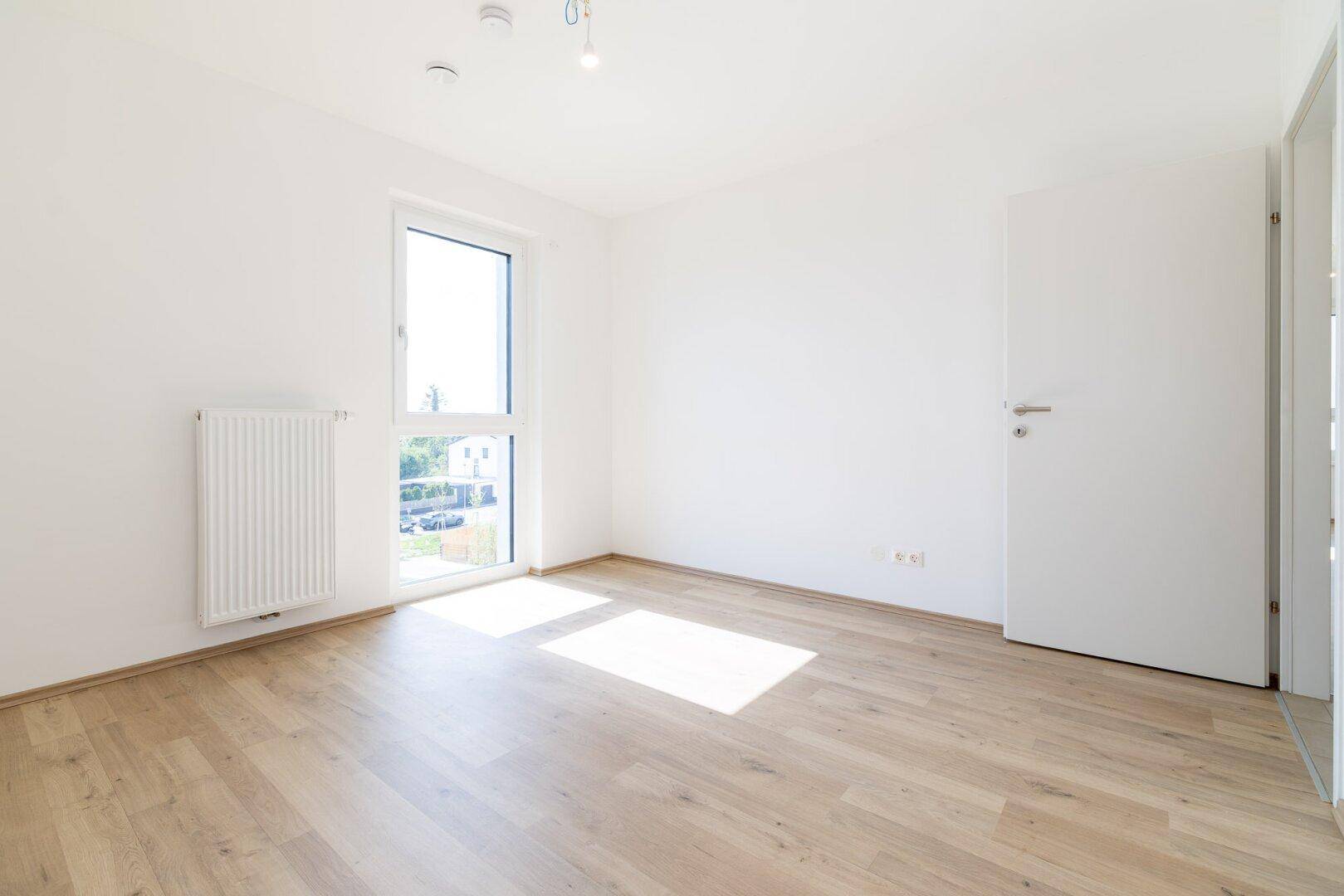 Freundliches Schlafzimmer mit Laminatboden und einem hohen Fenster, das den Raum erhellt.
