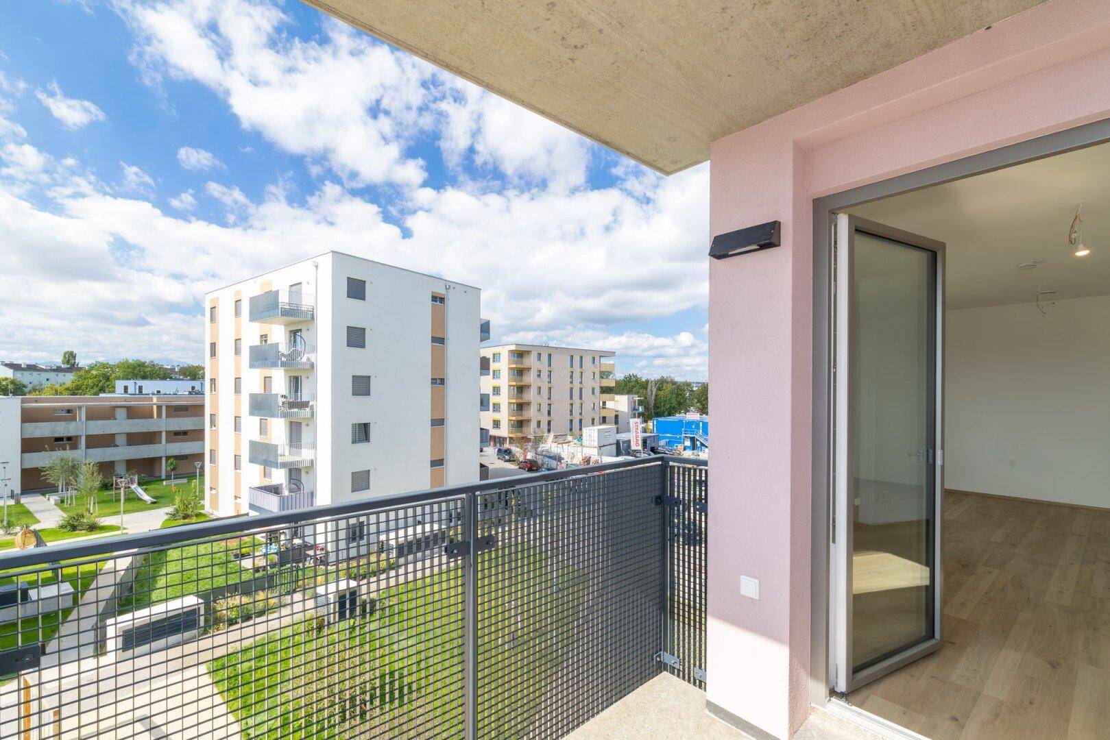 Blick vom Balkon auf moderne Wohngebäude und grüne Innenhöfe unter blauem Himmel.