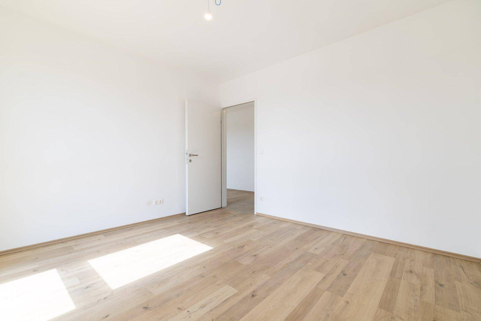 Leeres Schlafzimmer mit Laminatboden und weiß gestrichenen Wänden, bereit zum Einzug.