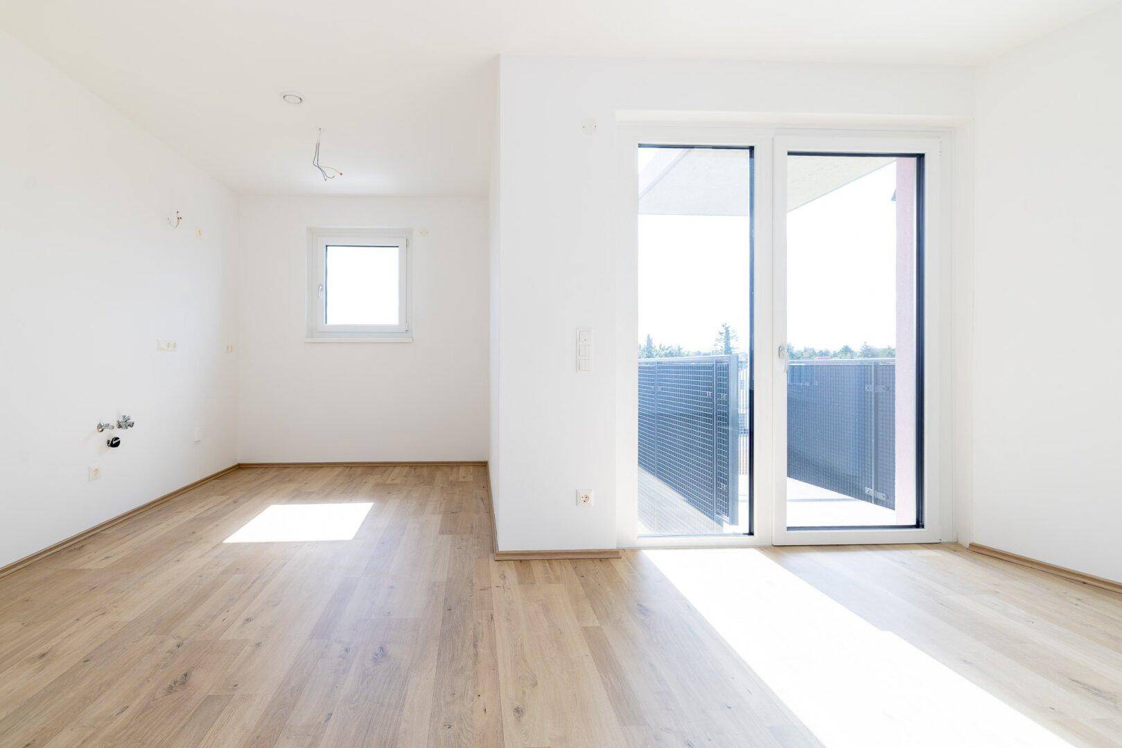 Lichtdurchfluteter Raum mit Balkonzugang und einem weiteren Fenster, ideal für ein Wohnzimmer.